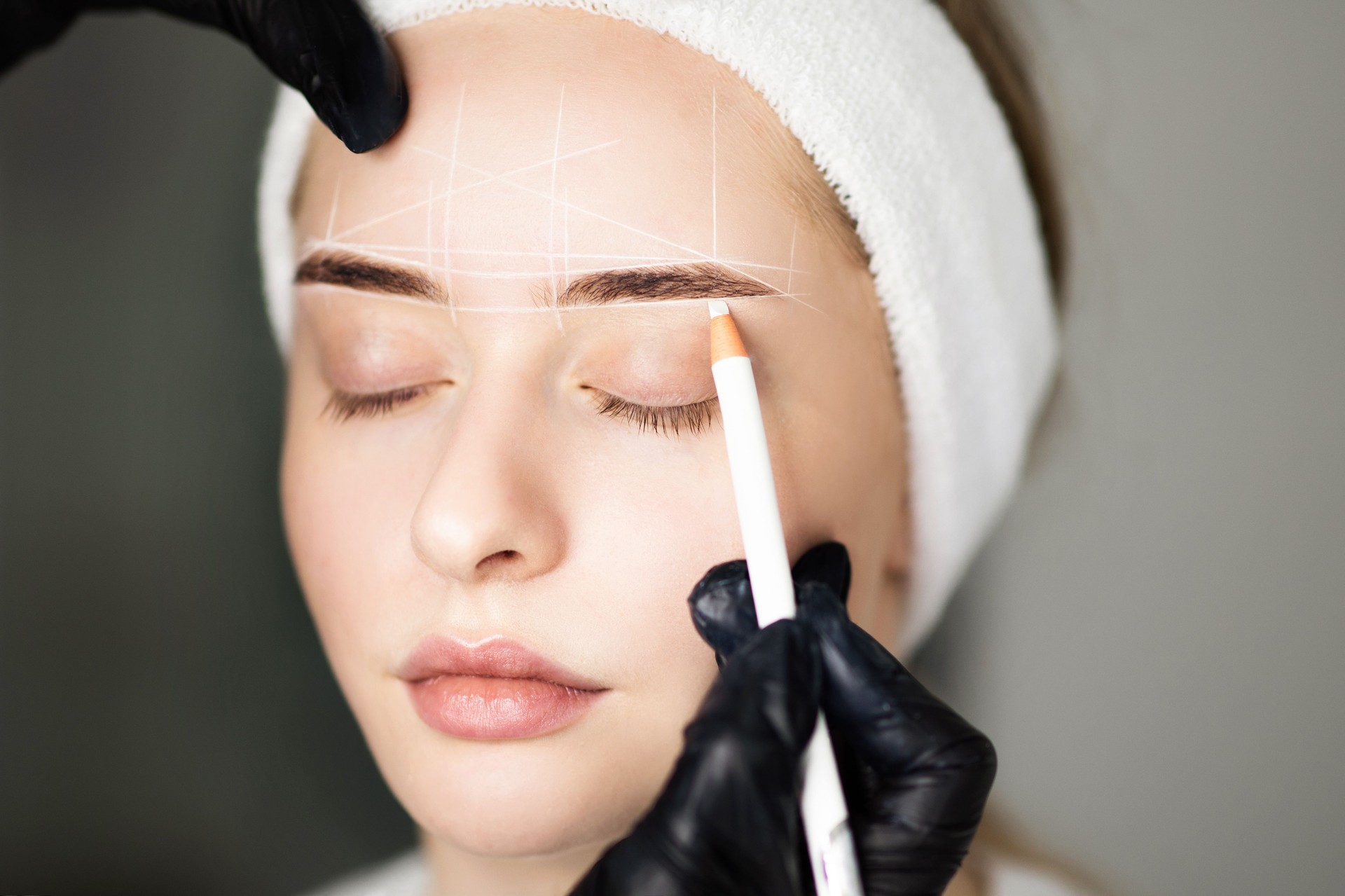 Cosmétologue cartographiant les sourcils d’une femme avec un crayon blanc avant le traitement de maquillage permanent